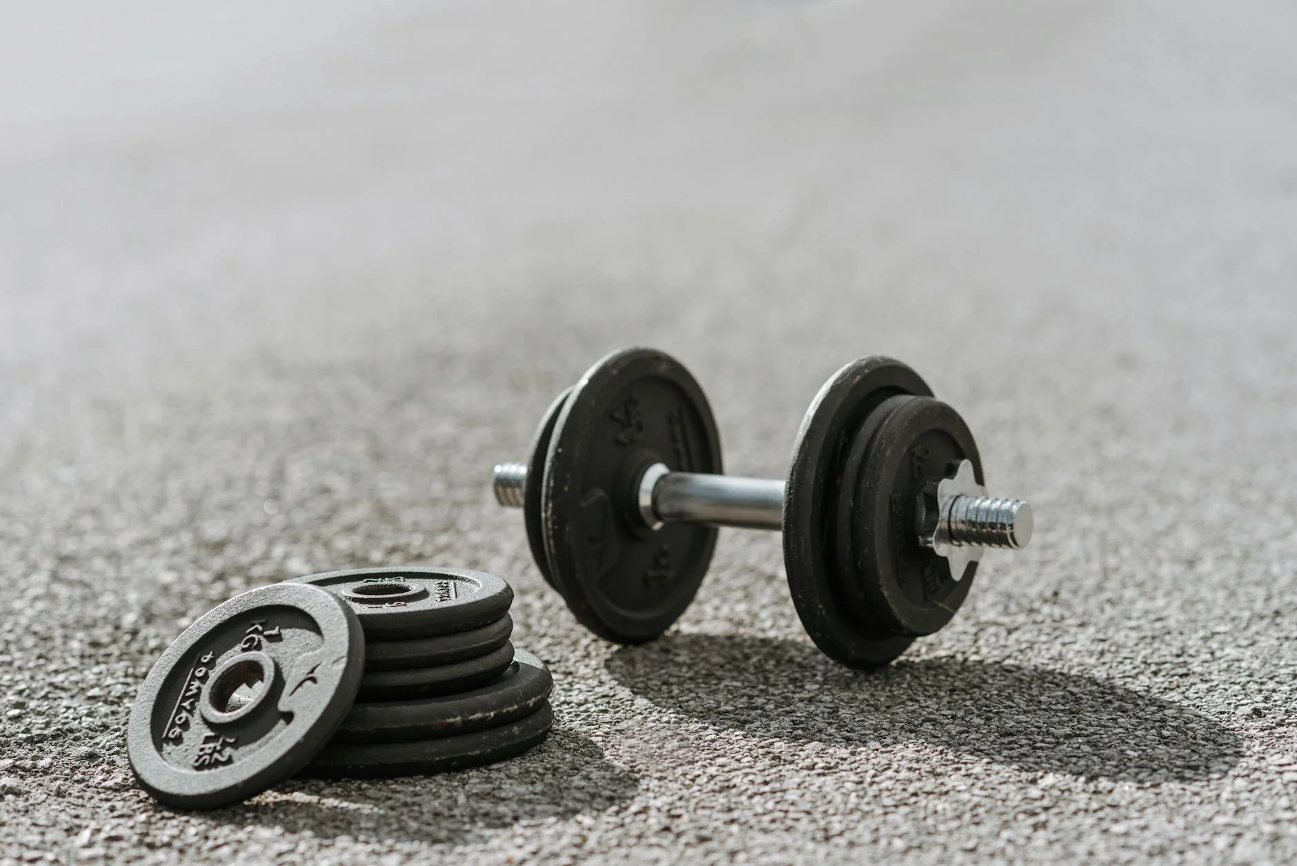 A black dumbbell and weights on an asphalt pavement, perfect for outdoor fitness themes.